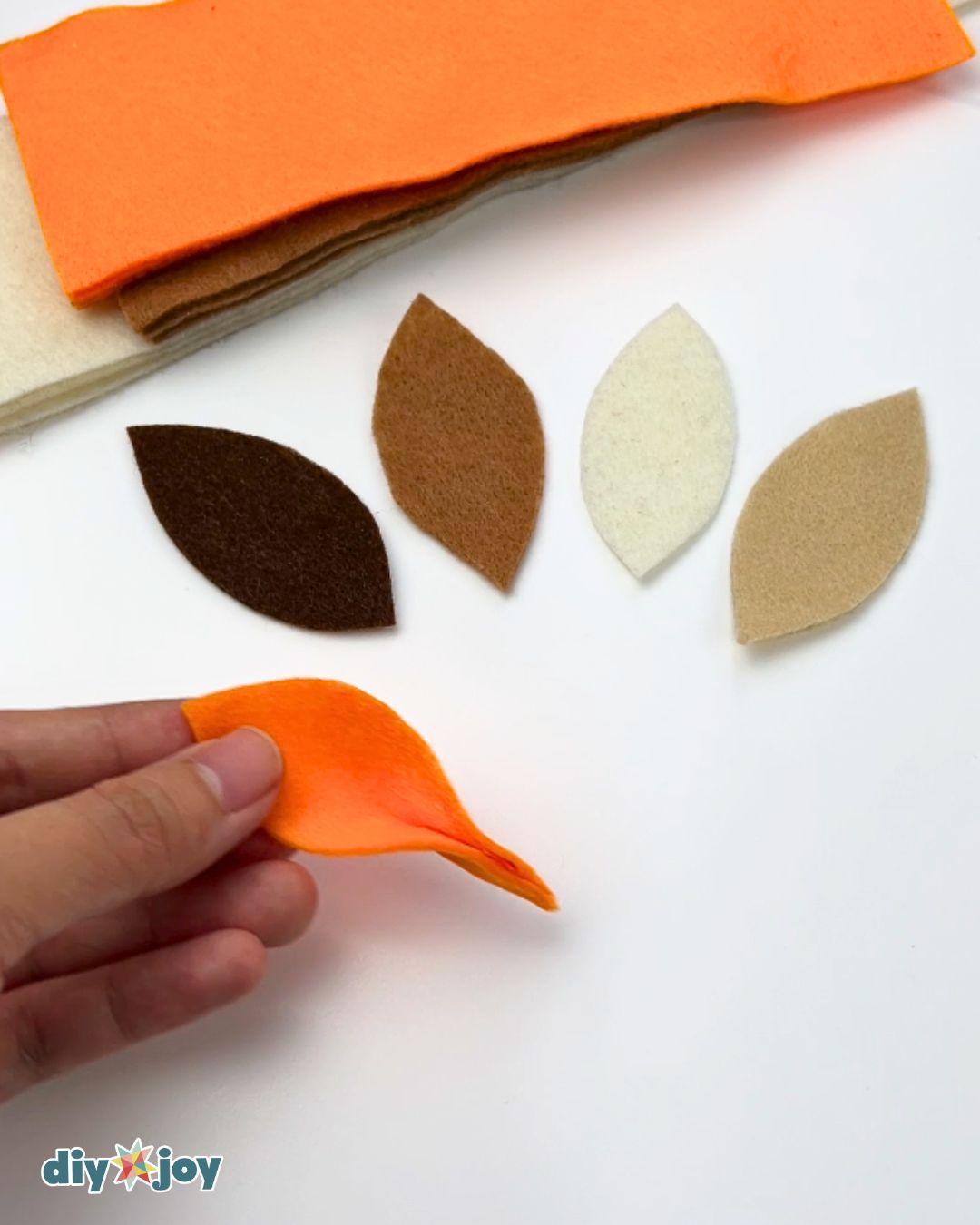 Felt crafts - folding and pinching a cut felt leaf beside sorted leaf shapes in brown, cream, and tan.