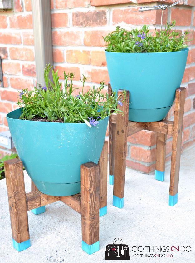 Two DIY plant stands in stained wood with blue dipped feet holding teal pots of lavender against a brick wall