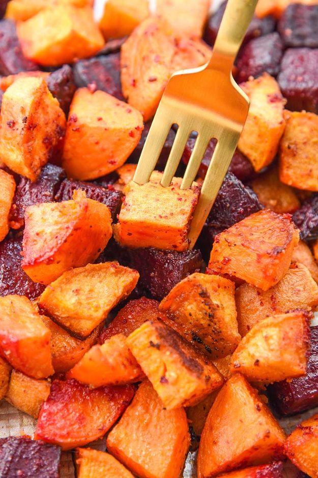Roasted beets and sweet potatoes cut in deep red and orange chunks on a parchment lined baking sheet