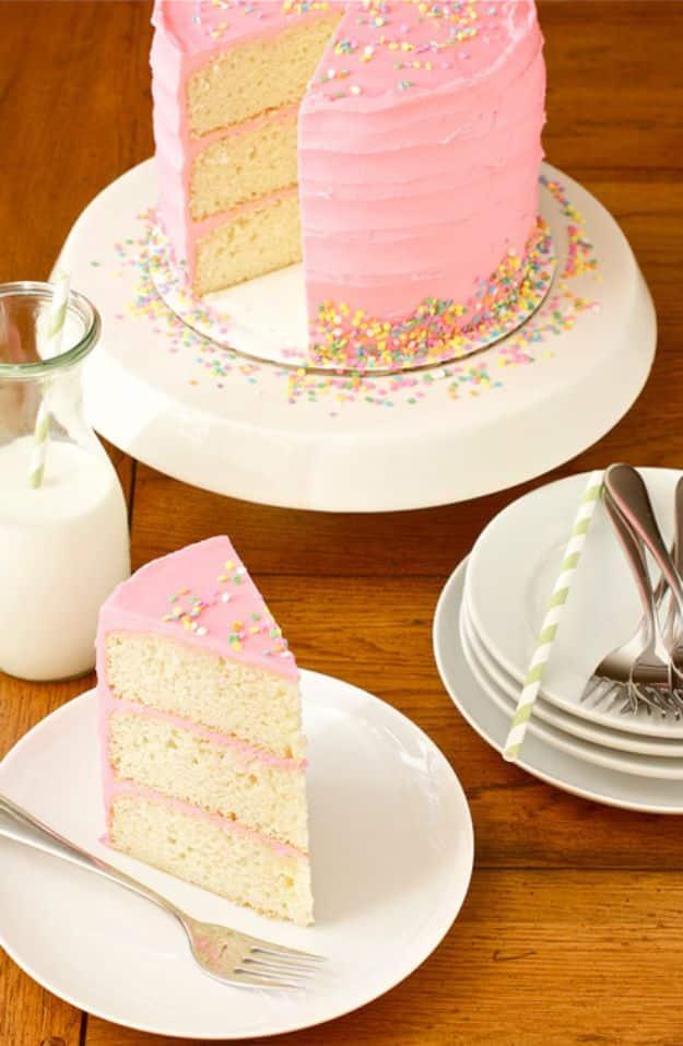 Pink frosted vanilla bean cake with a slice cut showing pale yellow layers and pink filling, sprinkles on the plate