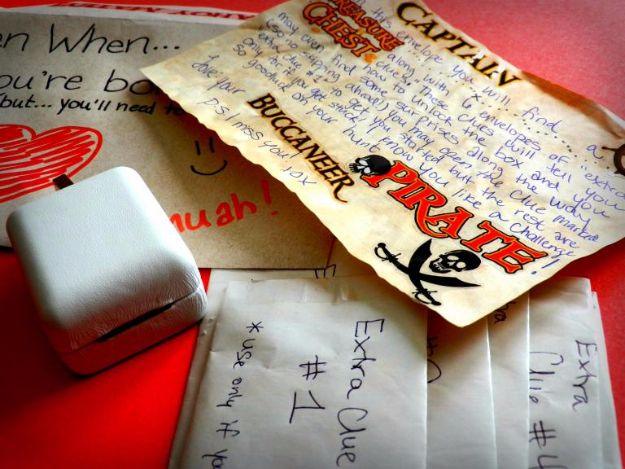 A long distance scavenger hunt gift laid out with aged paper clues, envelopes and a small locked box