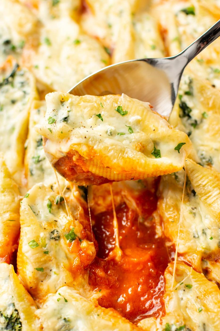 A spoon lifting a spinach and ricotta stuffed shell from a dish of melted cheese and red marinara sauce