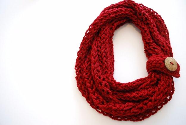 Deep red finger knit infinity scarf coiled into a figure eight with a knitted wrap and wooden button closure