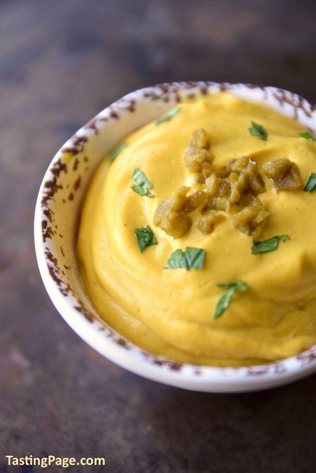 Vegan cauliflower queso, a smooth golden dip in a speckled bowl topped with chopped jalapeno and basil
