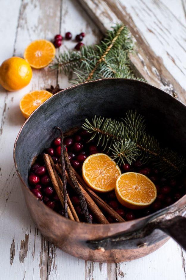 Copper pot of cranberries, orange slices, cinnamon sticks and pine sprigs on white wood for a holiday simmer pot