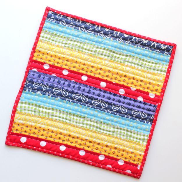 Rainbow mini quilt made from thirteen bright fabric strips with red polka dot binding on a white background