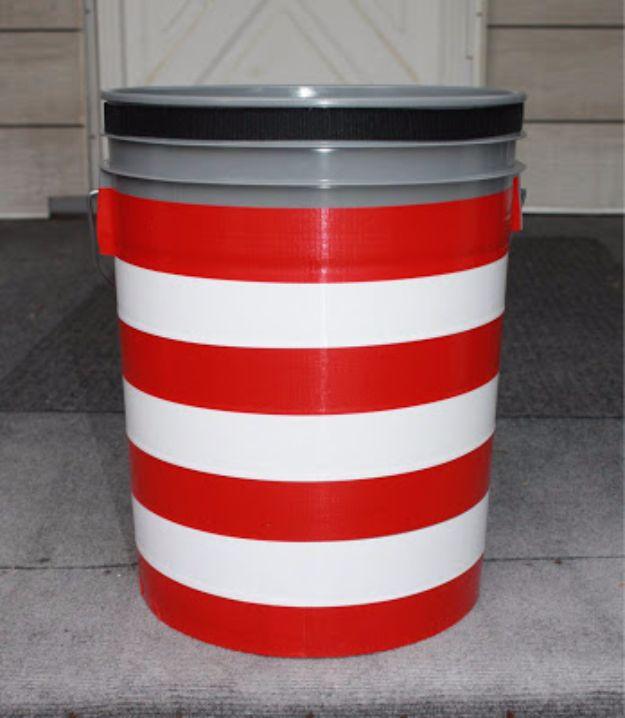 Five gallon bucket wrapped in red and white duct tape stripes with a gray lid clipped on top, standing on concrete