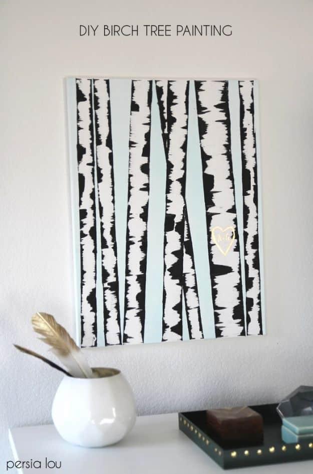 Canvas painting of black and white birch tree trunks on a white ground, beside a white vase of dried grasses