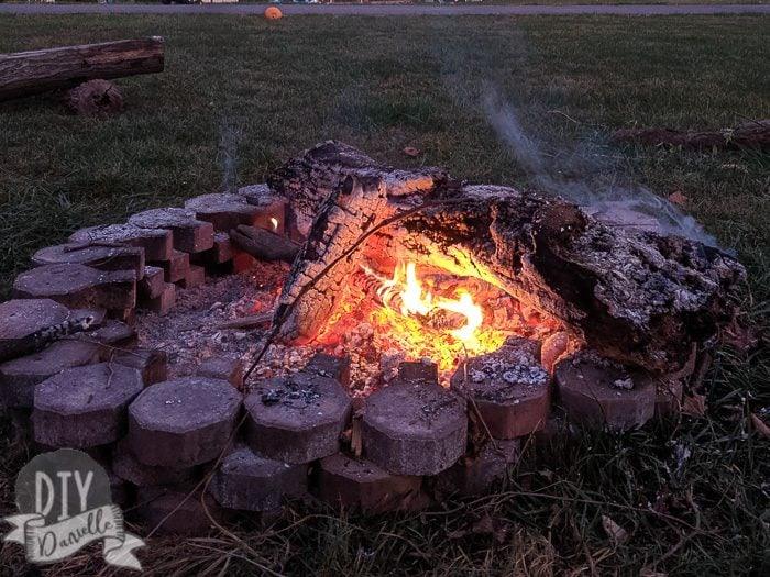 Free DIY fire pit area, a fire burning inside a ring of round leftover concrete blocks laid straight onto grass at dusk