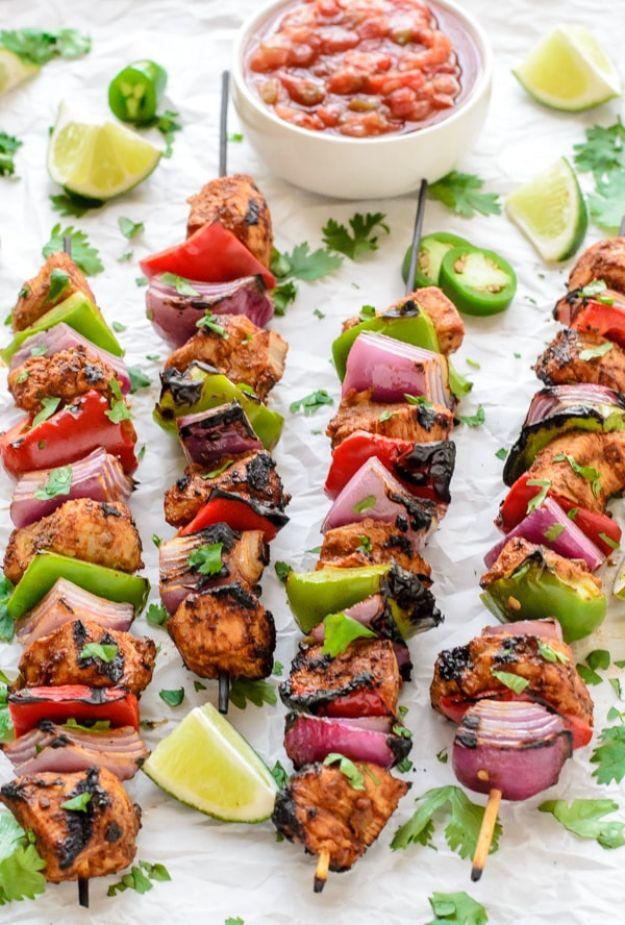 Fajita chicken kebabs on skewers with red and green peppers and red onion, salsa, lime wedges and cilantro