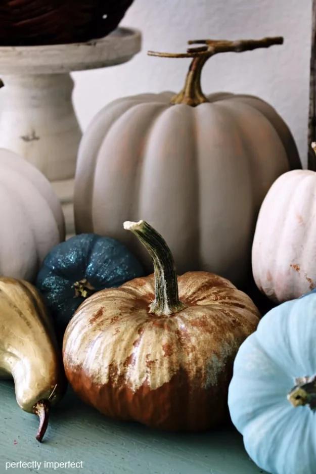 Group of chalk painted pumpkins in white, linen, blue and gold styled on an entry table with dried wheat