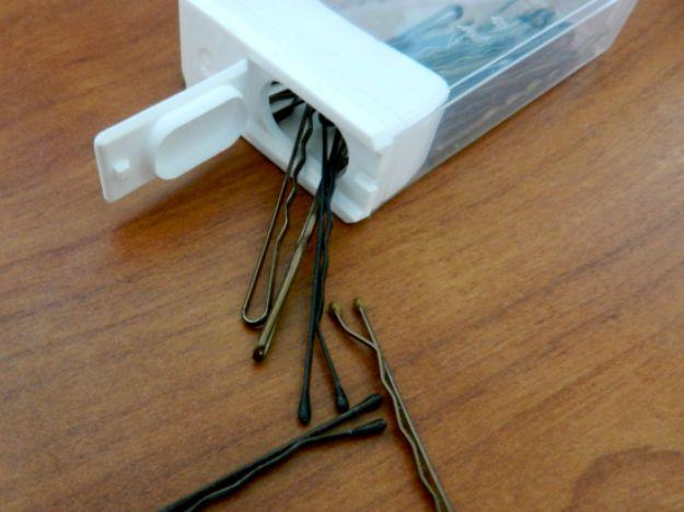 Tic Tac box reused as a bobby pin case, a clear flip top box with dark bobby pins spilling onto a wooden table
