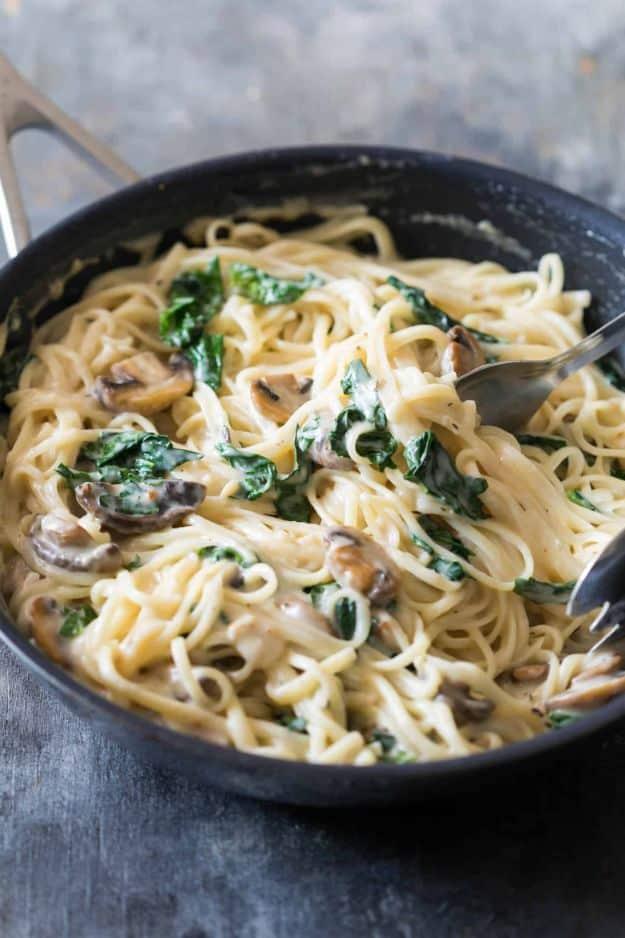 Creamy lemon mushroom kale linguine tossed in a dark skillet with wilted greens and sliced mushrooms