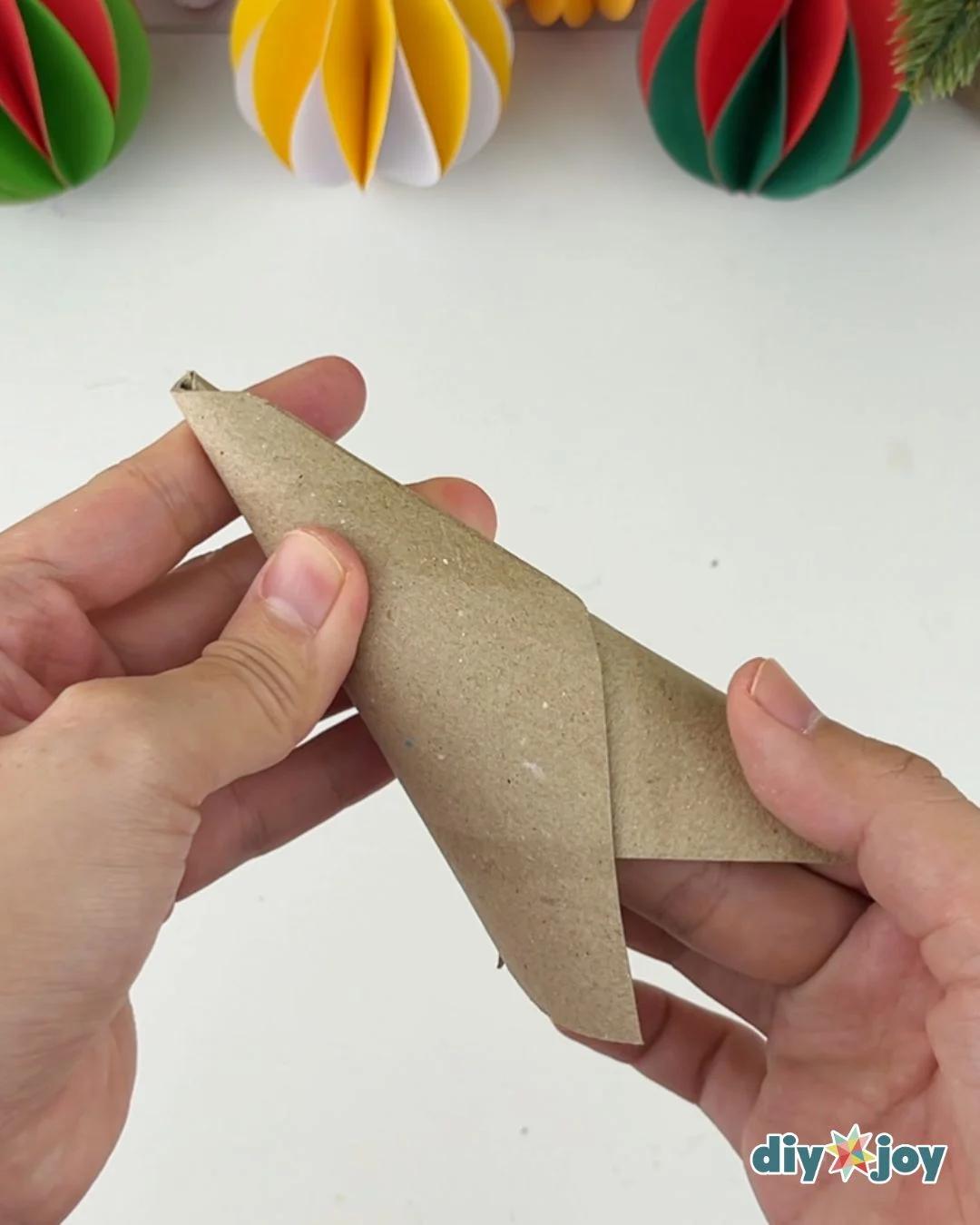 DIY Cardboard Crafts - two hands roll a flattened piece of brown cardboard diagonally into a cone shape on a white table