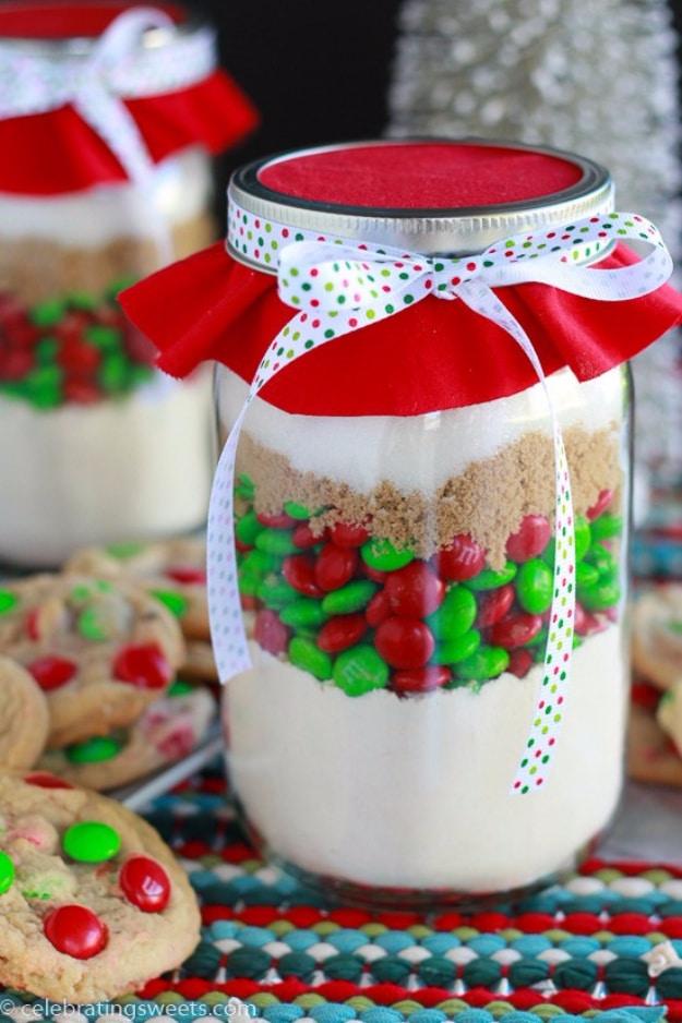 Quart mason jar layered with red and green M&M cookie mix, tied with ribbon beside a plate of cookies