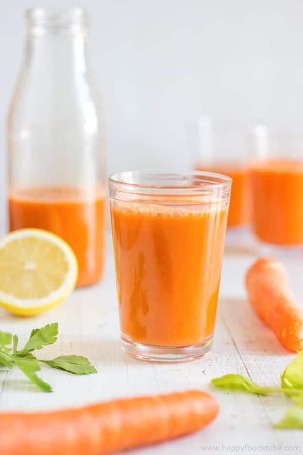 Winter vitamin boosting juice in a glass with whole carrots, a halved lemon and parsley on white wood