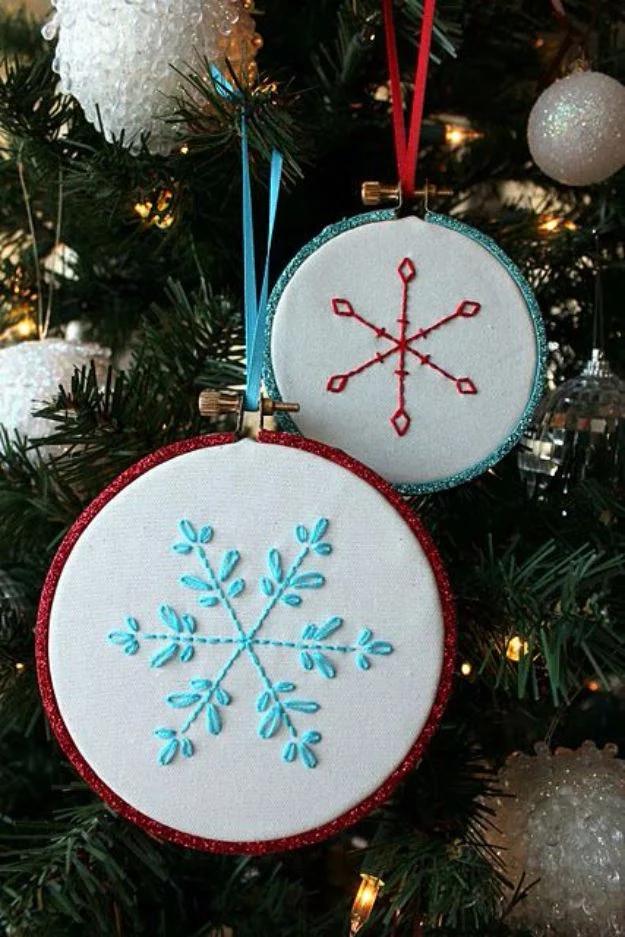 Two embroidery hoop ornaments on a lit Christmas tree, one red rimmed and one turquoise, each with a stitched snowflake