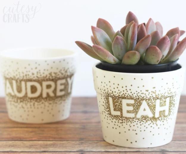 Sharpie dot flower pot craft, two white ceramic pots dotted in gold with names left clear in the dots, holding a succulent