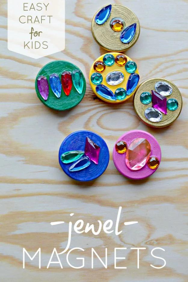 Painted wooden circle magnets covered in jewel tone acrylic paint and colorful craft gems on a wood table