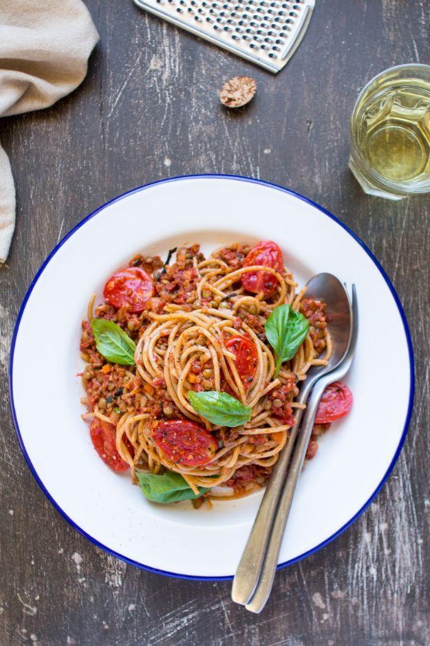 Vegan bolognese spaghetti with lentils and halved cherry tomatoes on a blue rimmed plate with fresh basil