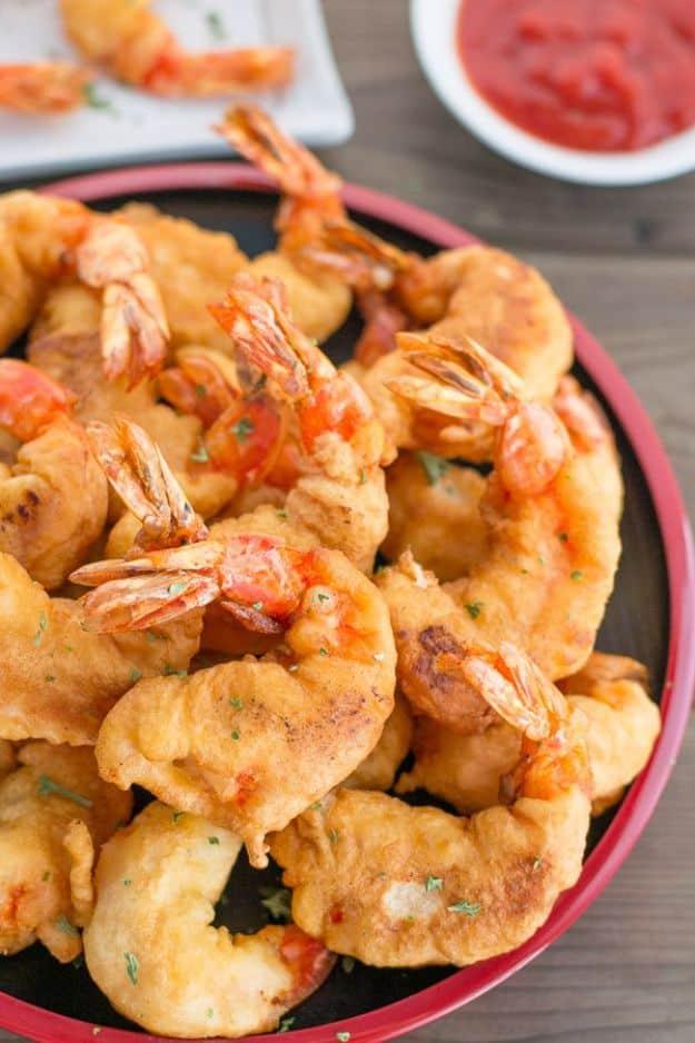 Camaron rebosado, golden battered prawns with tails piled on a platter with a bowl of red dipping sauce