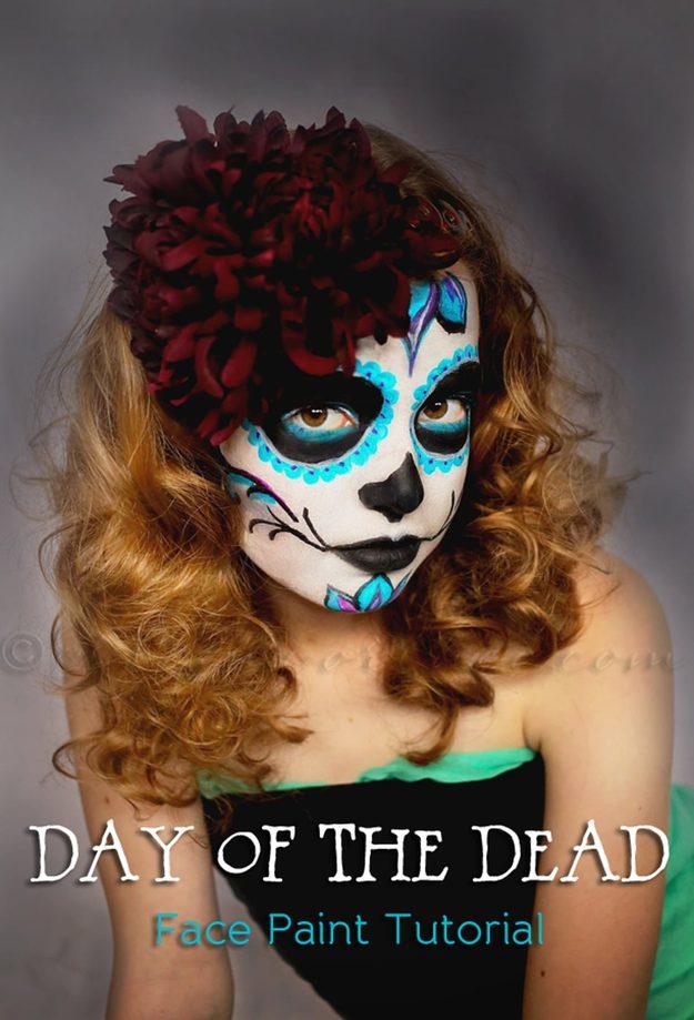Sugar skull Halloween makeup with blue petal eye shapes, black face paint and red flowers in long curled hair