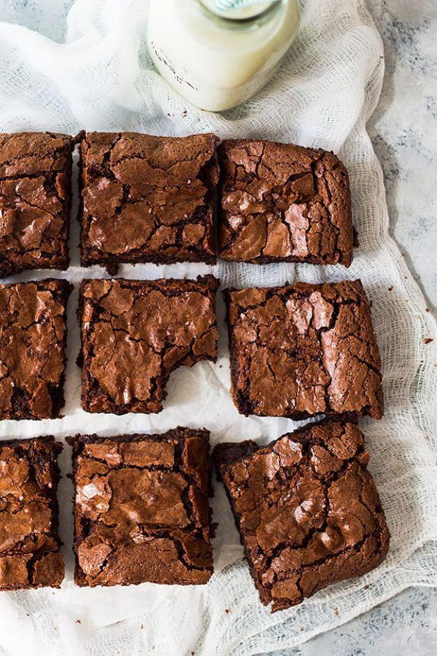 Nine chewy brownie squares on white parchment over marble with a mint lidded glass milk bottle behind them