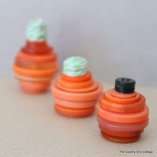 Three mini pumpkins made from stacked orange buttons with twine stems, one topped with a black button