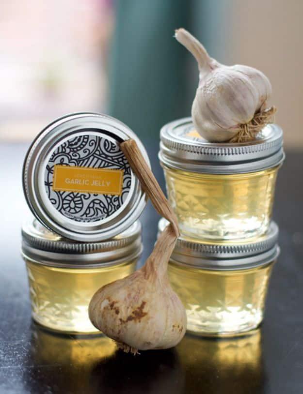 Roasted garlic jelly in small four ounce canning jars, pale gold, with roasted garlic heads and rosemary