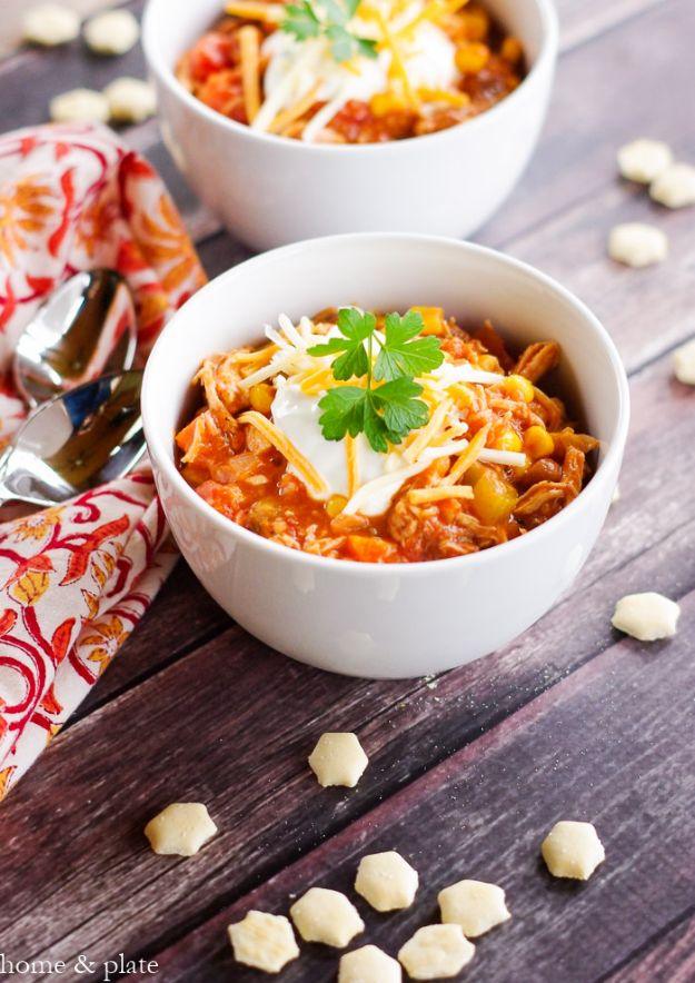 Two white bowls of buffalo chicken chili with sour cream and parsley beside scattered oyster crackers