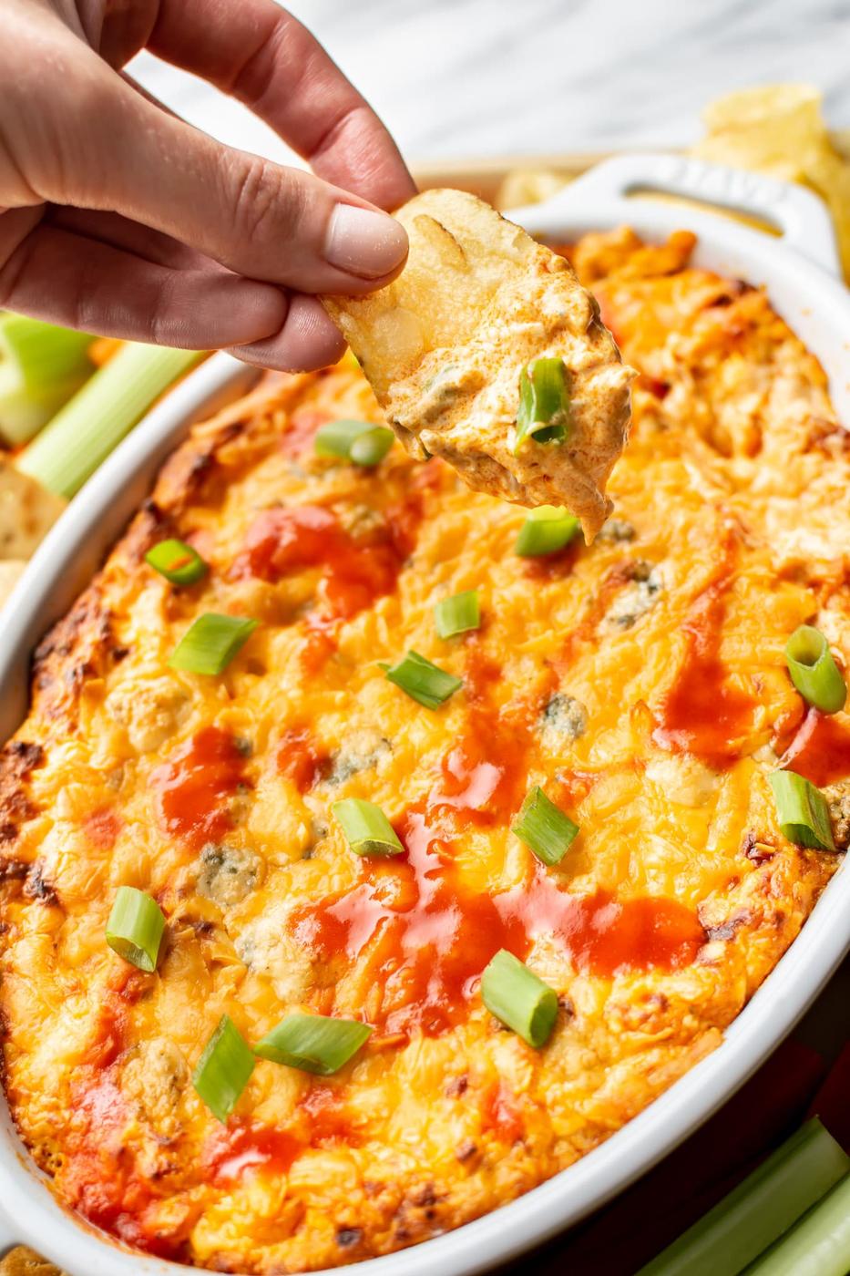 Buffalo chicken dip bubbling in a skillet with melted cheddar on top and green scallions scattered over