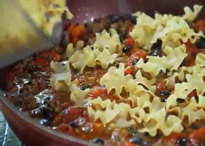Adding the egg noodles to the beef taco skillet
