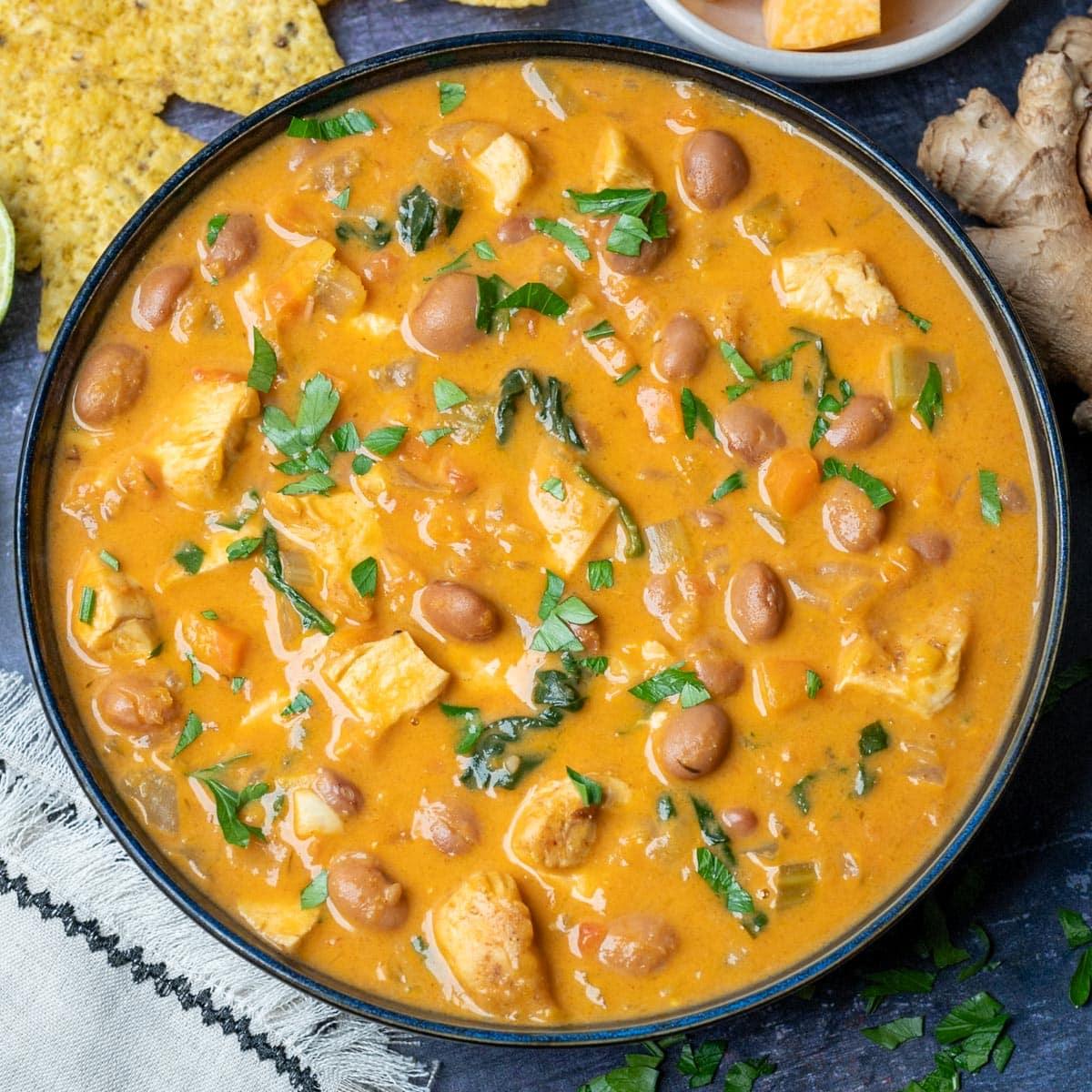 Chicken pumpkin soup in a dark rimmed bowl with beans and parsley, tortilla chips standing in the creamy broth