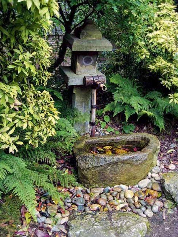 Stone lantern and a low carved tsukubai stone water basin with a bamboo spout among ferns and pebbles