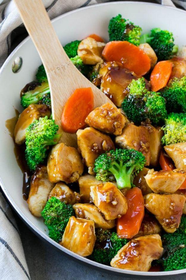 Honey garlic chicken stir fry in a white skillet with broccoli florets, sliced carrots and a wooden spoon