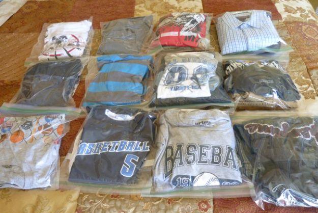 Flat lay of a child's clothes, each outfit sealed in its own clear ziploc bag, laid out on a patterned bedspread