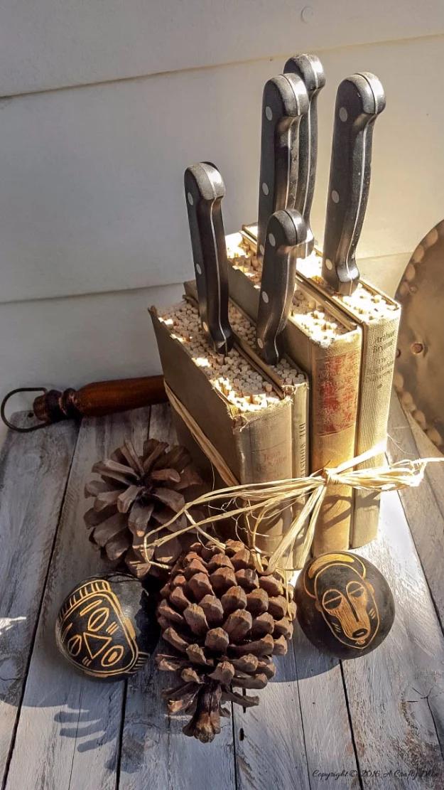 Knife block made from old books with black handled knives slotted in, styled on a wooden counter with pine cones