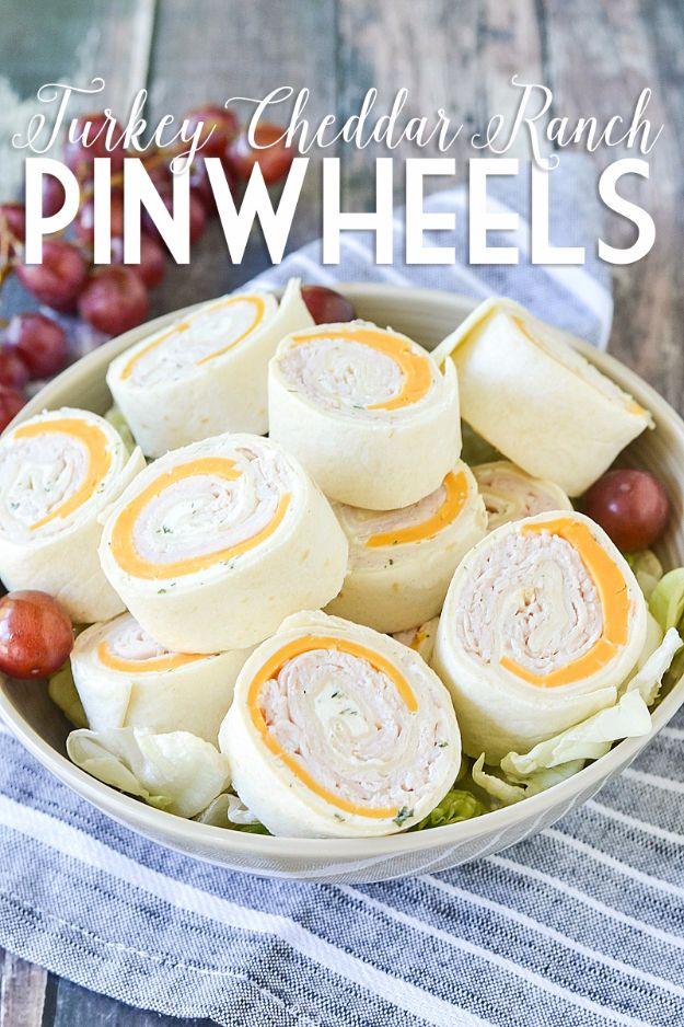Turkey cheddar ranch pinwheel slices stacked in a white bowl with red grapes on a striped linen napkin
