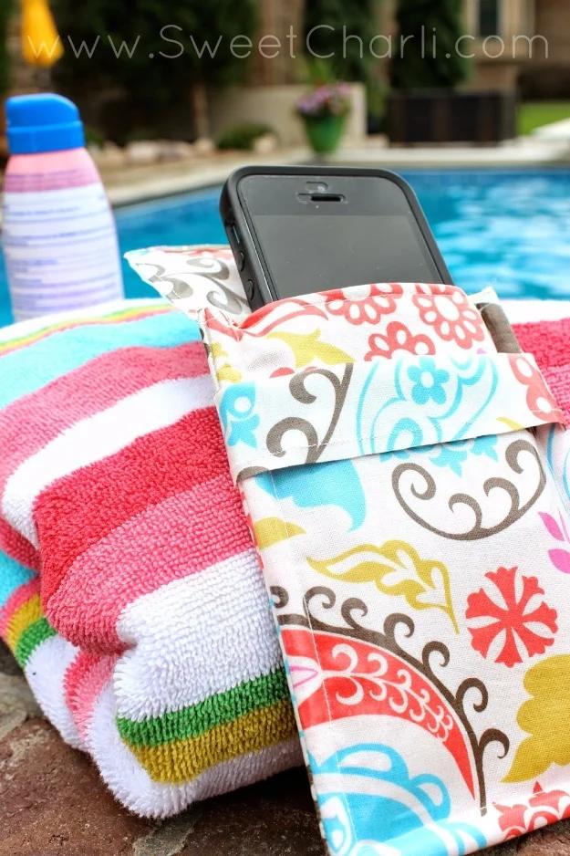 Cream and coral print phone pouch with a fold over flap, resting on a striped beach towel beside a pool
