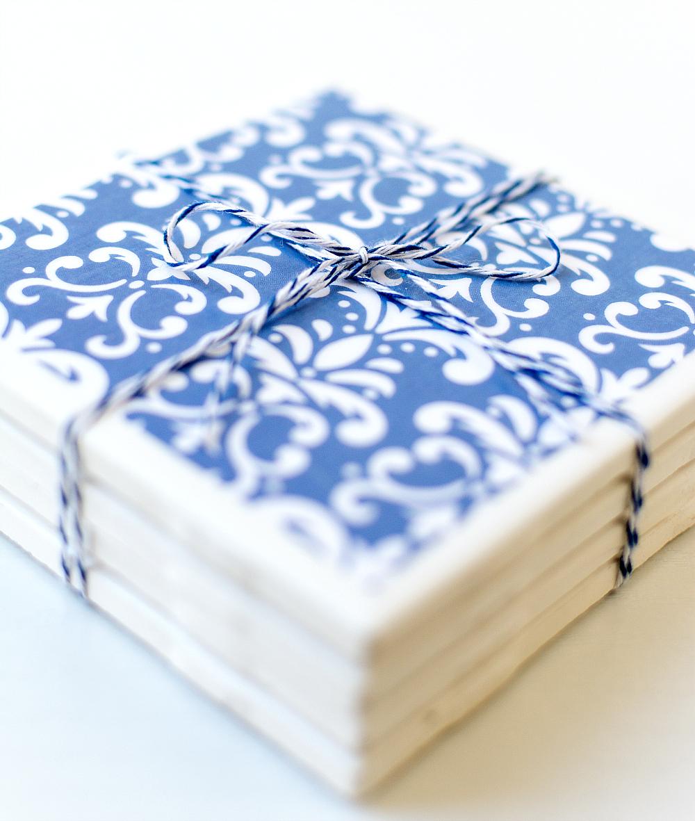 Stack of white tile coasters covered in blue and white damask scrapbook paper, tied up with navy twine