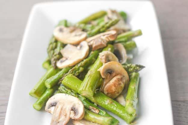 Roasted garlic asparagus and mushrooms on a white rectangular dish with green spears and sliced mushrooms
