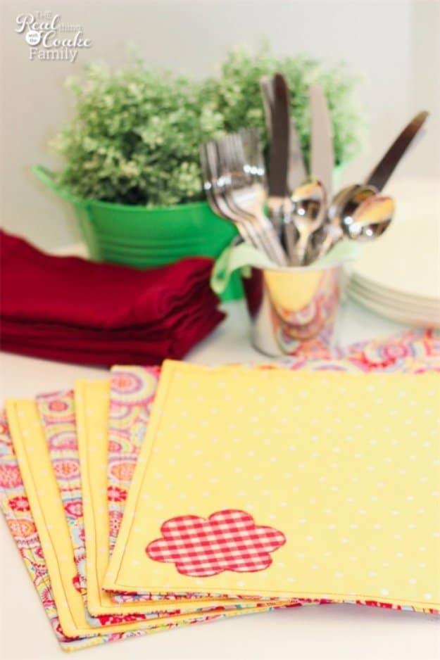 Two stacked reversible placemats in blue and cream floral cotton on a bare wooden table, sewing crafts that sell in sets.