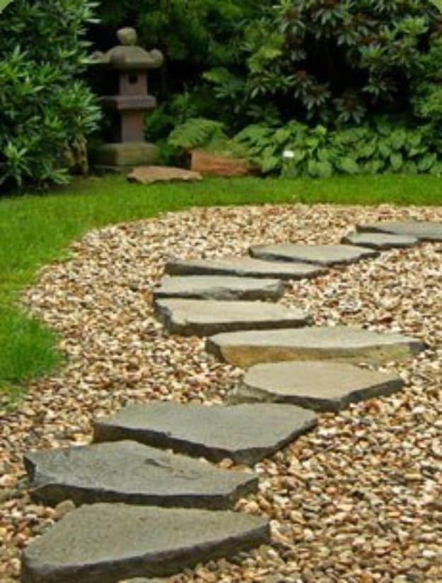 Irregular flagstones set at walking stride spacing through pale gravel, past a stone lantern and shrubs