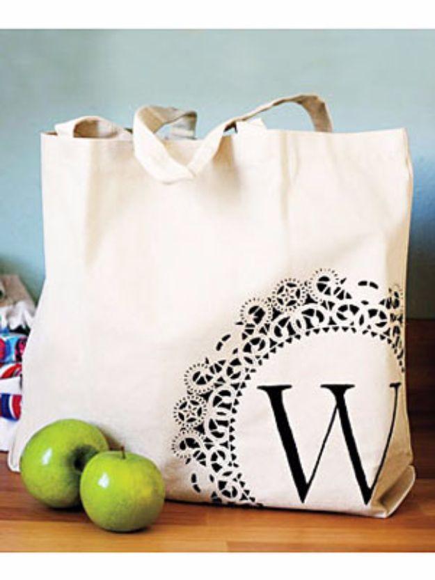 Canvas tote bag stenciled with a black doily pattern and the letter W, standing beside two green apples