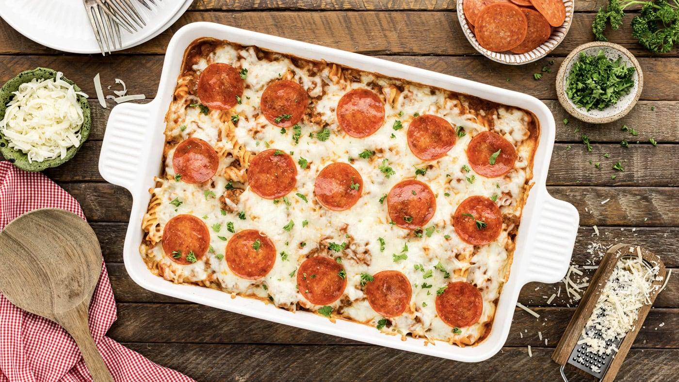Pepperoni pizza pasta casserole in a white baking dish, melted mozzarella covered with rounds of pepperoni