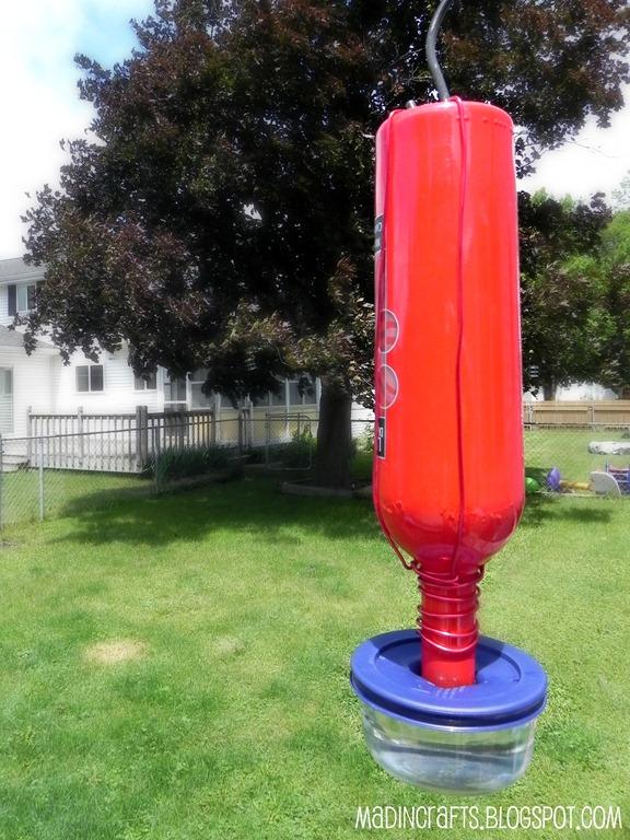 Wine bottle hummingbird feeder, a red bottle upside down in a blue lidded bowl hanging in a green yard