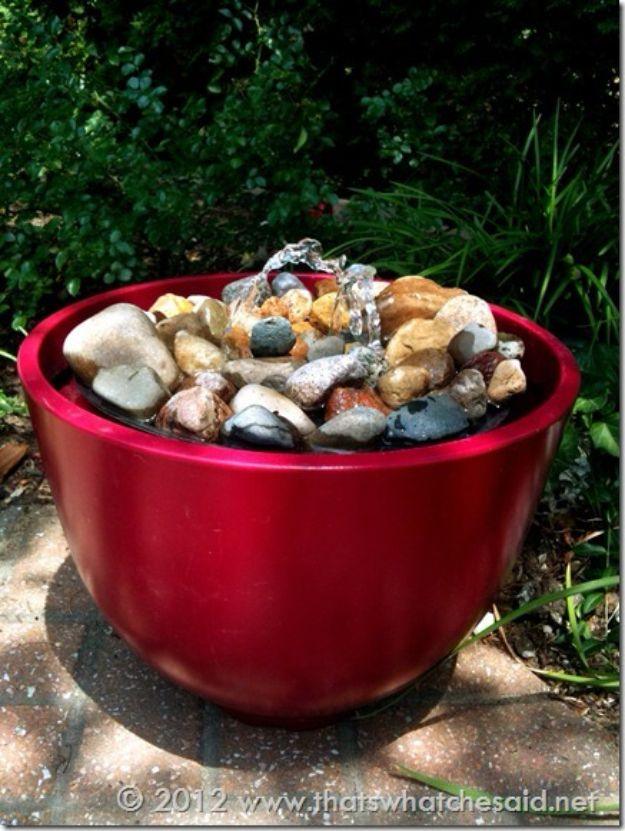 Red metallic bowl planter filled with river stones and two bubbling spouts standing on a brick patio