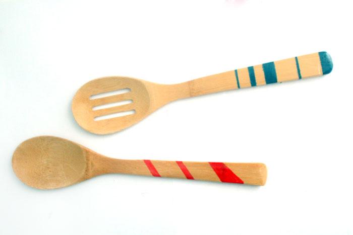 Two bamboo wooden spoons with teal and coral striped handles laid side by side on a plain white surface