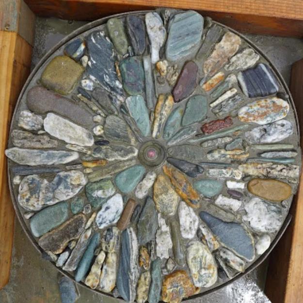 Round pebble mosaic stepping stone in a wooden form, stones set on edge in a radiating pattern around a center