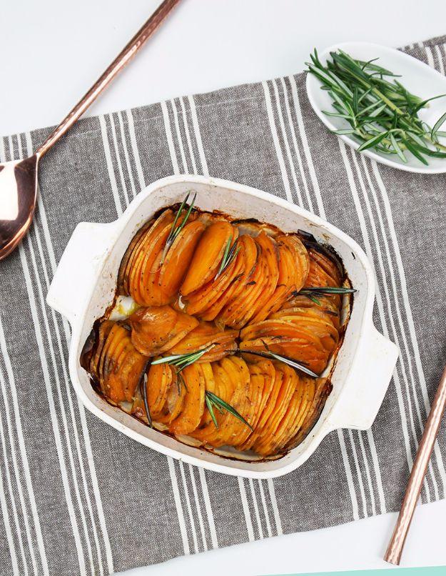 Roasted hasselback sweet potatoes standing on edge in a baking dish with shallot slices and rosemary